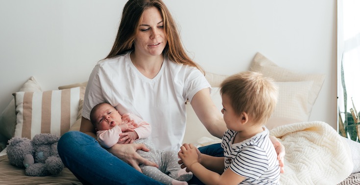 Mother holding a baby and sitting with a young child Mother holding a baby and sitting with a young child